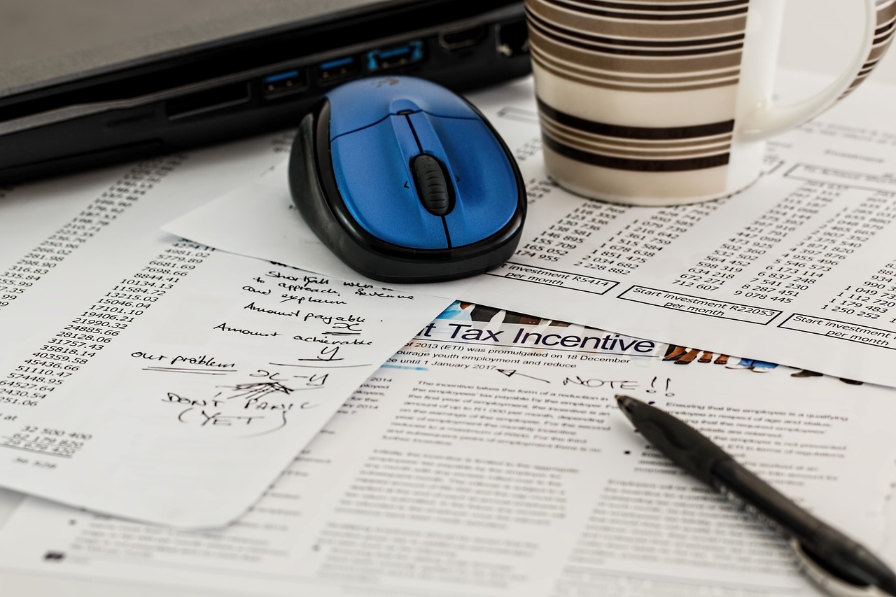A tax withholding form and a pay stub lying on a desk next to a pen.