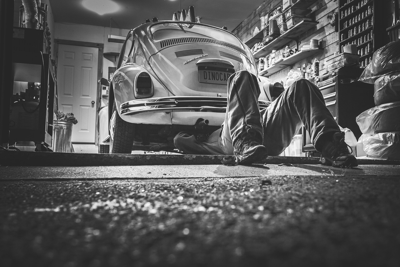 A mechanic inspecting the underside of a car in a repair shop.