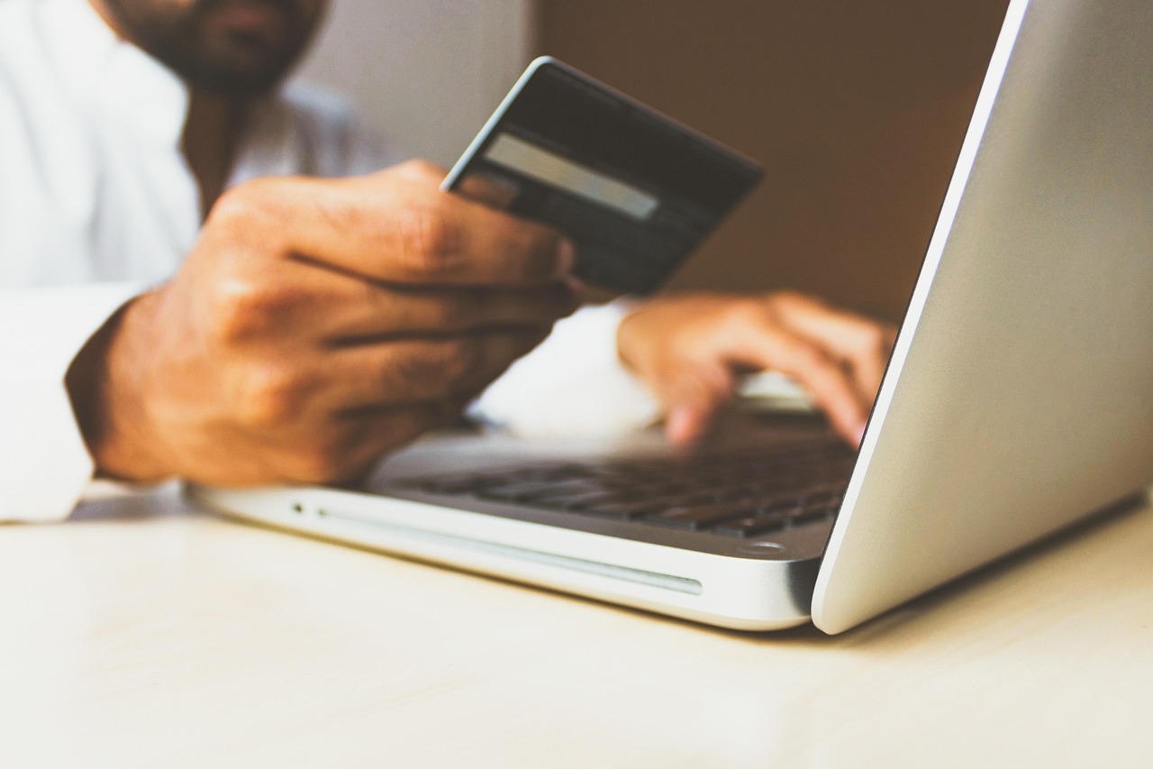 A person's hands holding a credit card next to a laptop showing an online account.