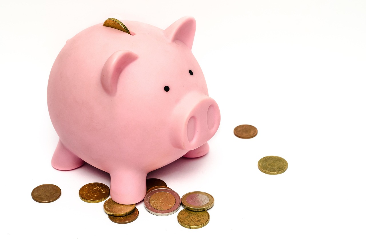 A piggy bank beside stacks of coins on a table.